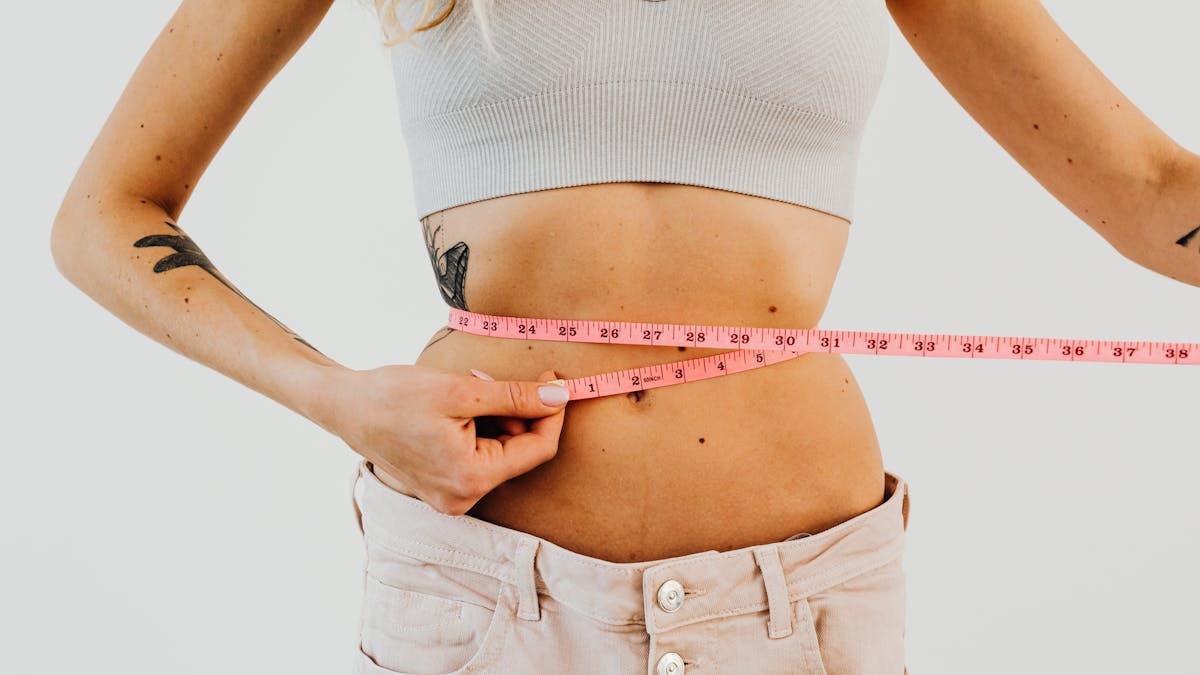 Close-up of woman in sports bra measuring waist with pink tape for fitness goals.